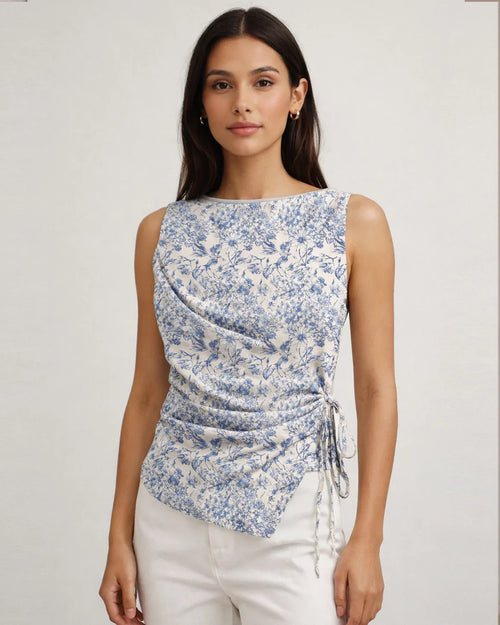 Women wearing blue and white floral sleeveless top with a boat neckline, asymmetrical hem, and side tie detail for a fitted, stylish silhouette