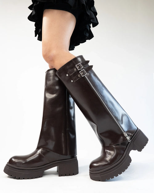 Front view of Brown knee high boots with glossy finish, side zipper, buckle detail, and chunky sole for a bold winter style.