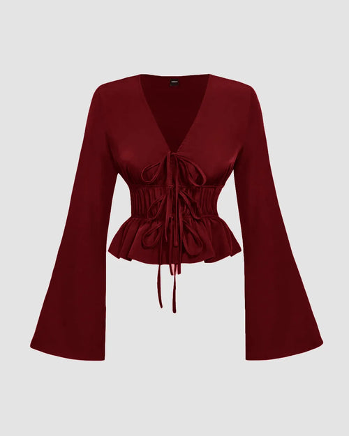 Front view of a red long sleeve top with a deep V-neck, tie-front ruching, and flared sleeves on a plain background.
