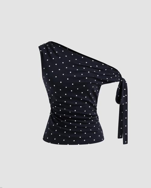 Front view of Black asymmetrical top with white polka dots, featuring ruched detailing and a side tie knot for a fitted, stylish silhouett