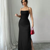 Front view of a woman wearing a black spaghetti strap maxi dress with a ruched fit, side slit, and crisscross back straps for an elegant evening look.
