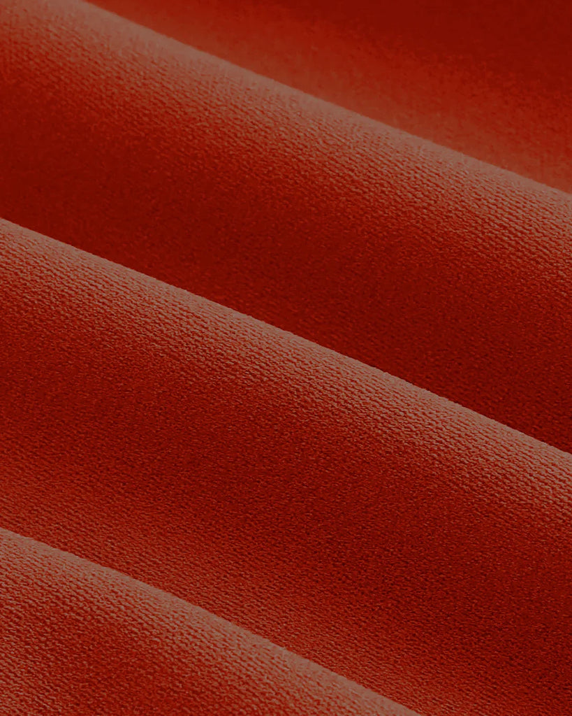 Closed view of a brick red maxi dress featuring a boat neck and a decorative bow at the neckline.