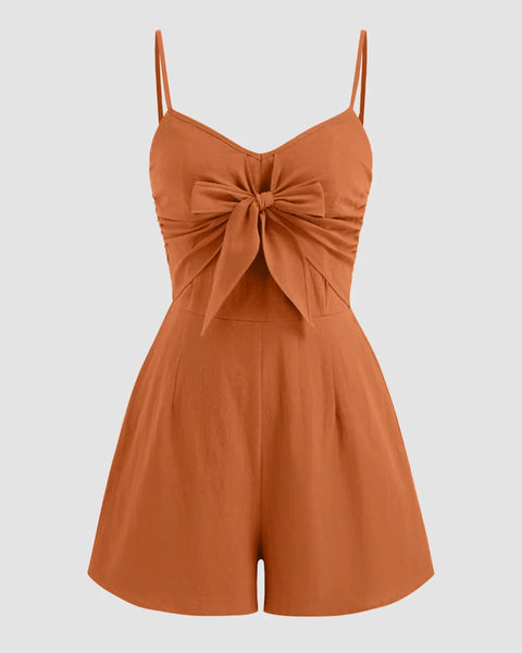 Front view of v neck jumpsuit in rust with spaghetti straps, bowknot front and flared shorts silhouette for a chic look.