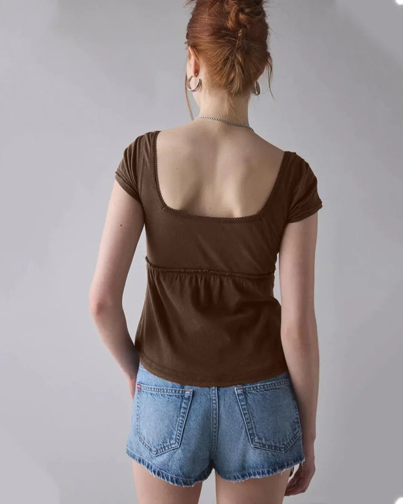 Back view of a woman in a brown button-front square neck top and shorts, standing confidently with a neutral background.
