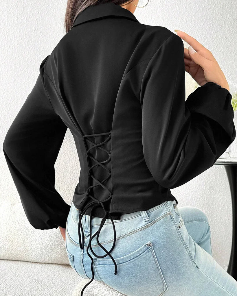 A woman wearing a fitted black collared button-down shirt and jeans stands confidently.