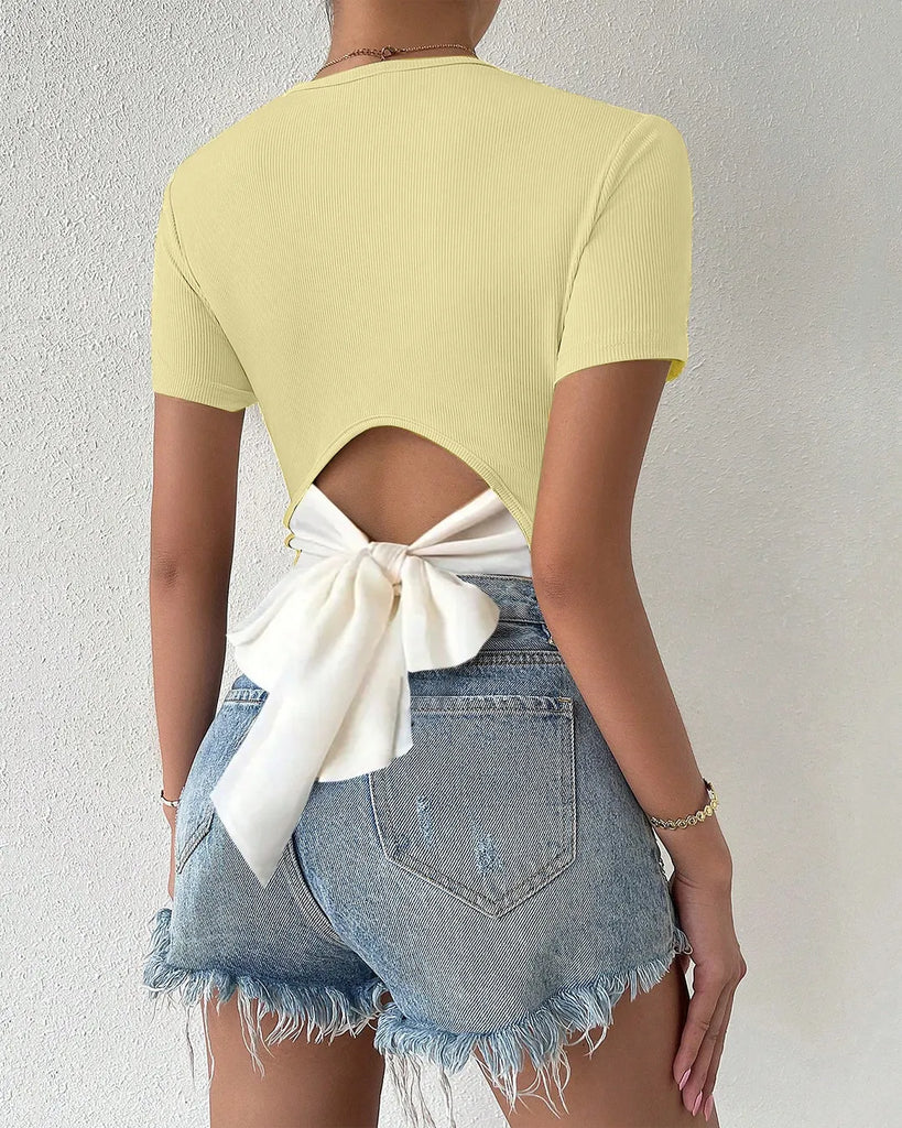 Woman's back view in a yellow top featuring a white bow, highlighting the Cut Out Bow Back Short Sleeve Top style.