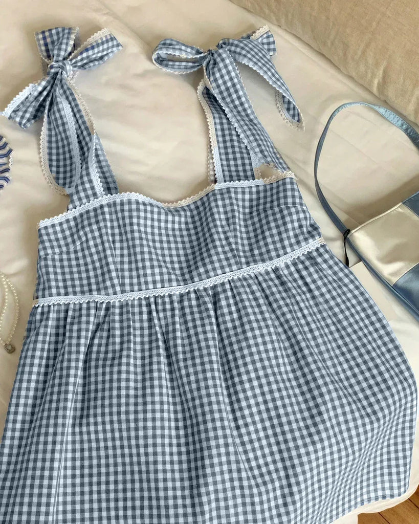 Blue and white gingham dress featuring bows on the back and sleeveless design, perfect for warm weather outings.
