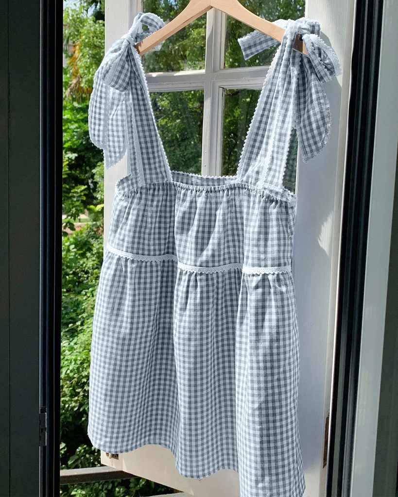 Blue and white gingham dress featuring bows on the back and sleeveless design, perfect for warm weather outings.
