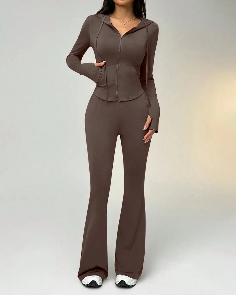 A woman in a brown sporty suit with a zippered hoodie takes a selfie, smiling at the camera.