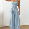  A woman in an ice blue sleeveless wide-leg jumpsuit stands confidently, showcasing a casual yet stylish look.
