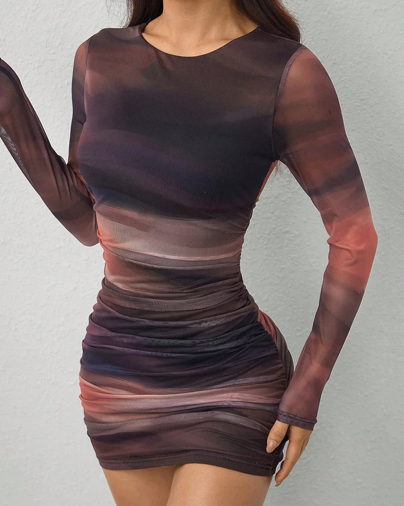  A woman poses for the camera in a long sleeve mesh print ruched bodycon mini dress and stylish boots.
