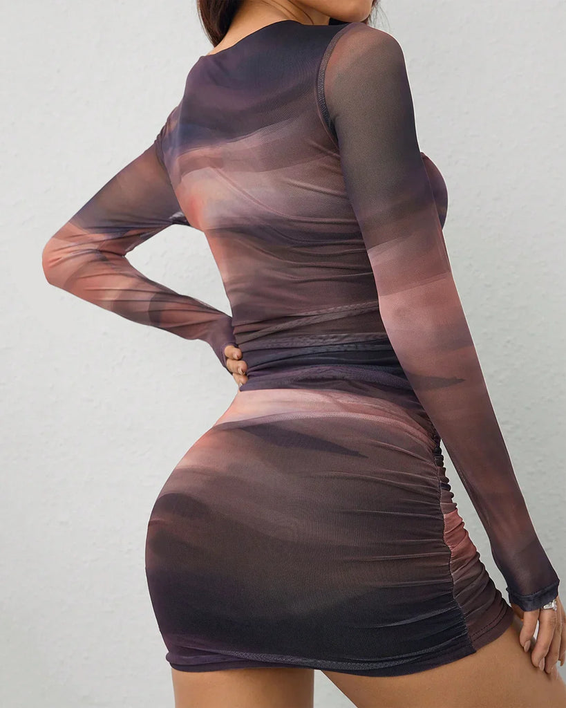 Back view of a woman poses for the camera in a long sleeve mesh print ruched bodycon mini dress and stylish boots.