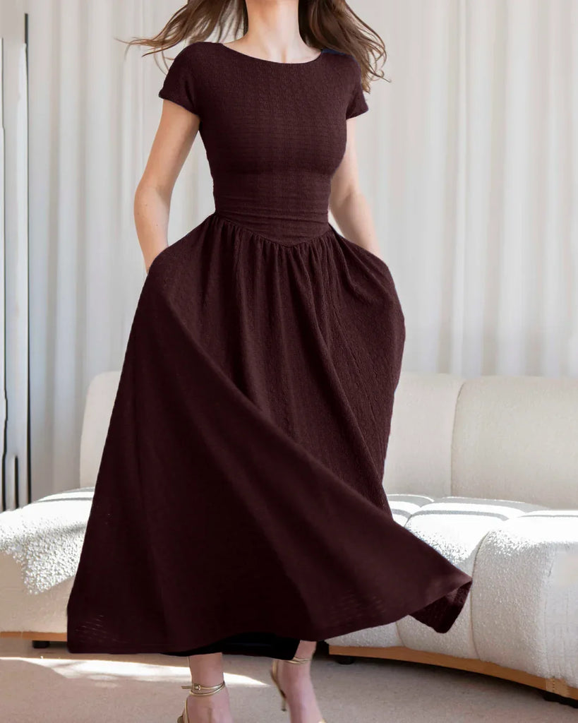 A woman poses in a maroon cap sleeve fit and flare midi dress, showcasing its elegant silhouette against a neutral background.