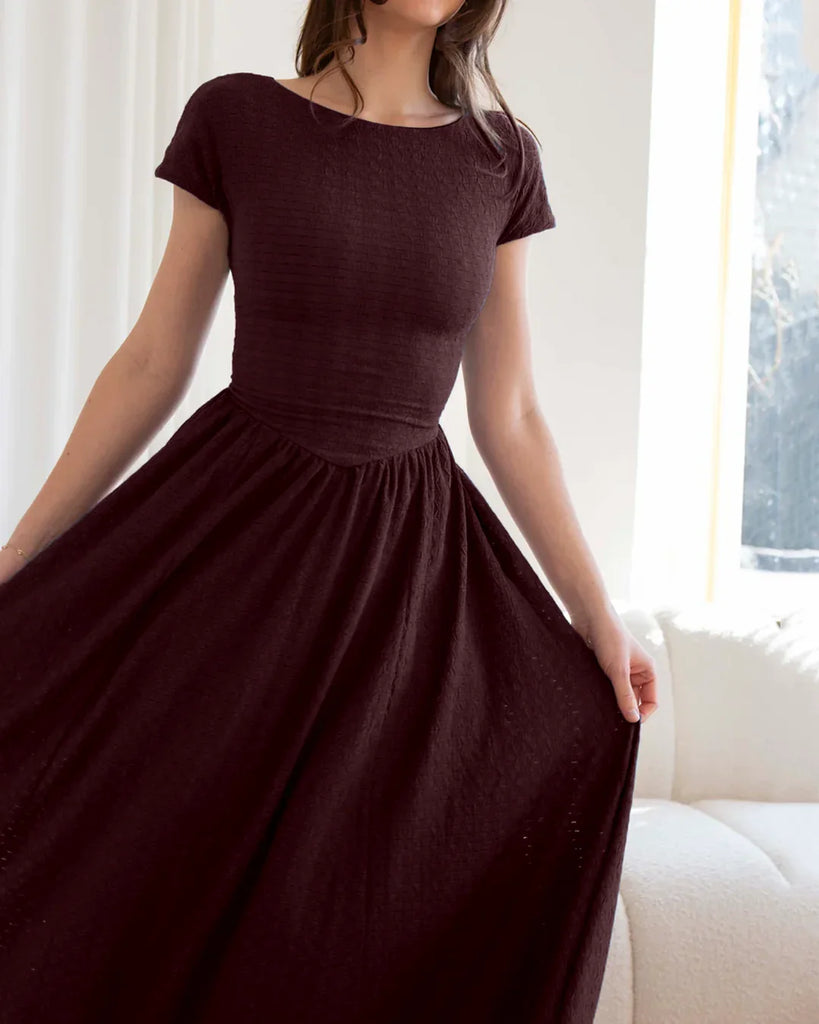A woman poses in a maroon cap sleeve fit and flare midi dress, showcasing its elegant silhouette against a neutral background.