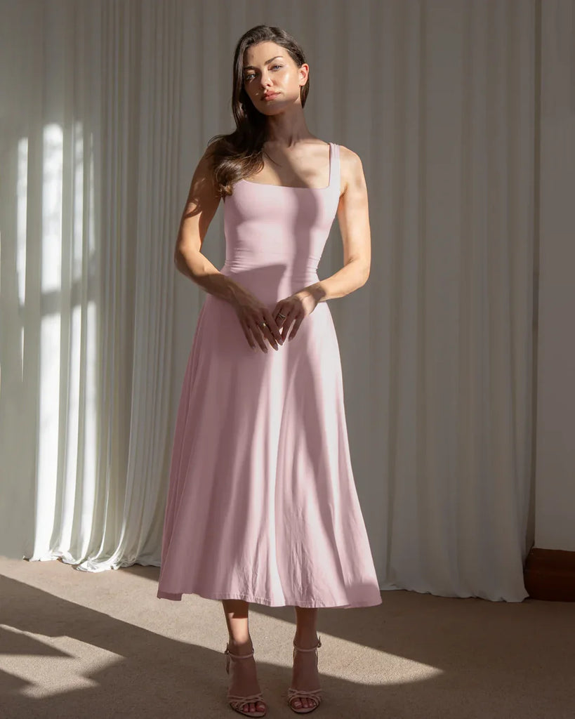 Model showcases a minimal fit and flare dusty pink midi dress, highlighting its elegant silhouette and soft color.
