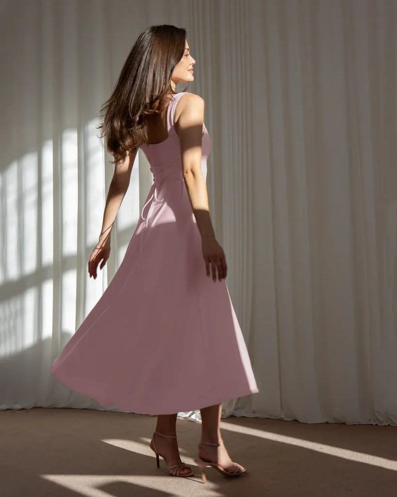 Model showcases a minimal fit and flare dusty pink midi dress, highlighting its elegant silhouette and soft color.
