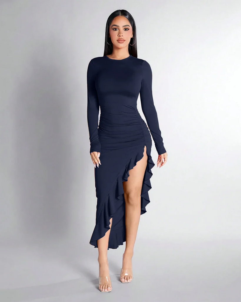 Model in a navy blue ruched dress with long sleeves and a high slit, featuring a ruffle hem.
