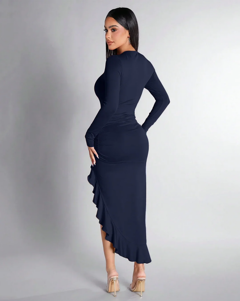 Back view of a Model in a navy blue ruched dress with long sleeves and a high slit, featuring a ruffle hem.