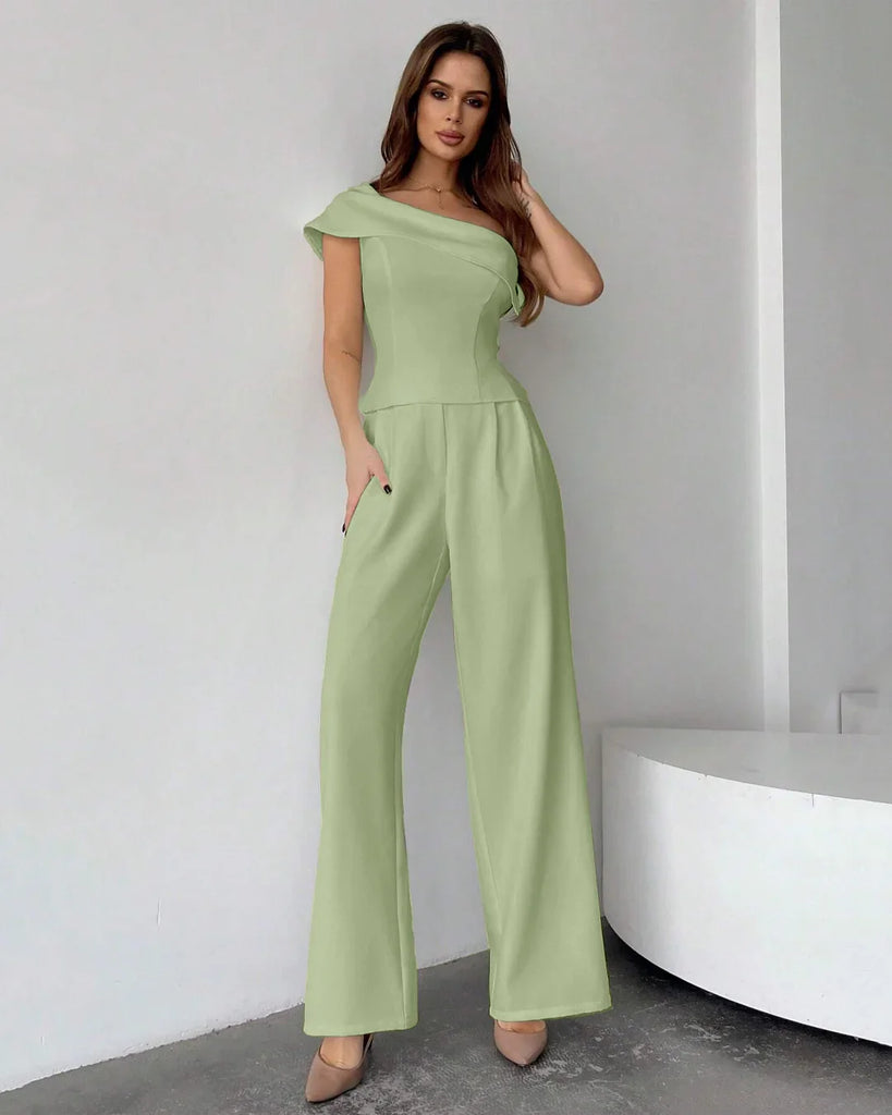 Model in a light pista green one-shoulder jumpsuit with draped top and wide-leg trousers, showcasing a stylish look.
