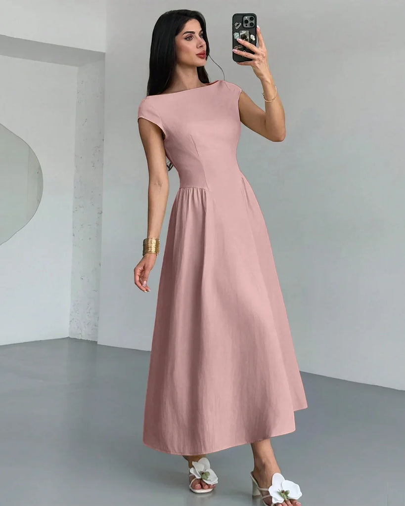 A woman in a powder pink one-shoulder flared hem midi dress takes a selfie, smiling at the camera.