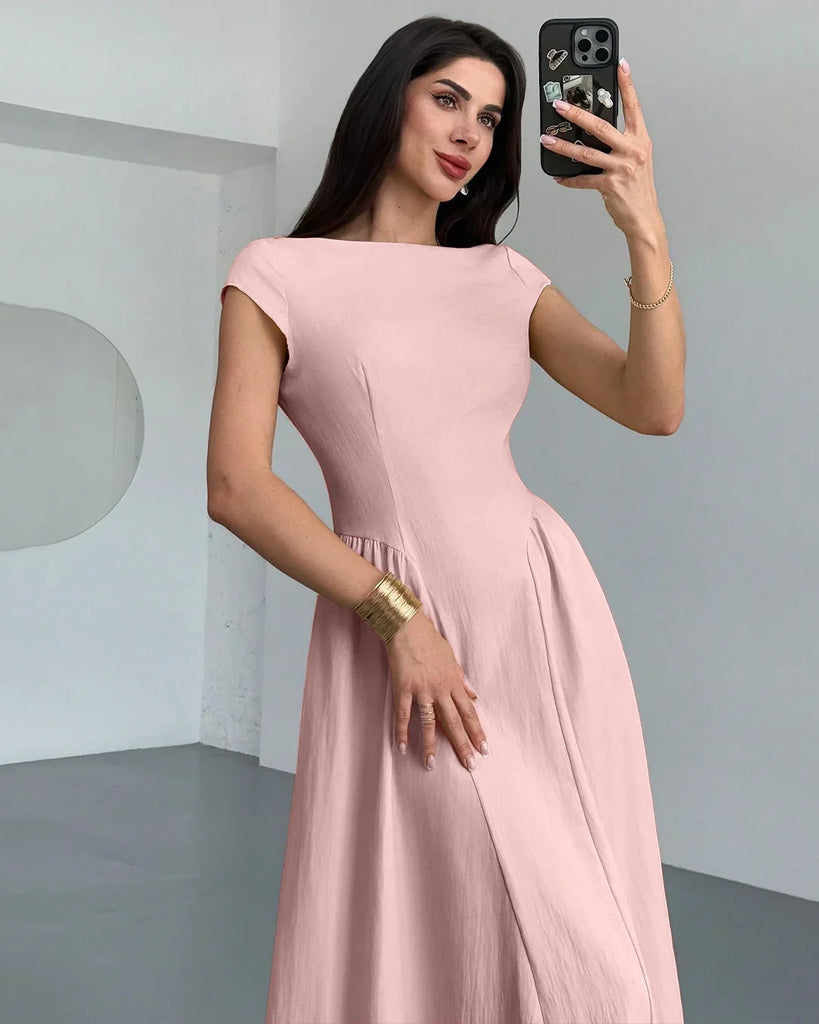  A woman in a powder pink one-shoulder flared hem midi dress takes a selfie, smiling at the camera.