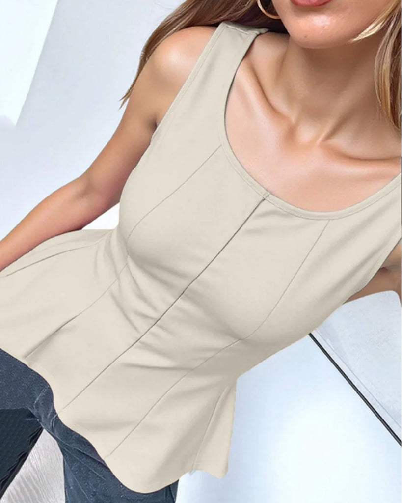 A woman in a fitted beige peplum top and jeans stands confidently, showcasing a stylish and casual outfit.