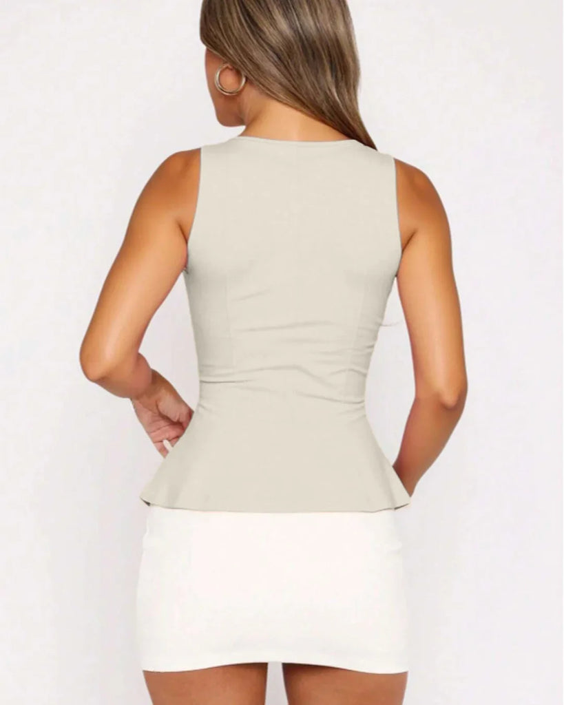 Back view of a woman in a fitted beige peplum top and jeans stands confidently, showcasing a stylish and casual outfit.