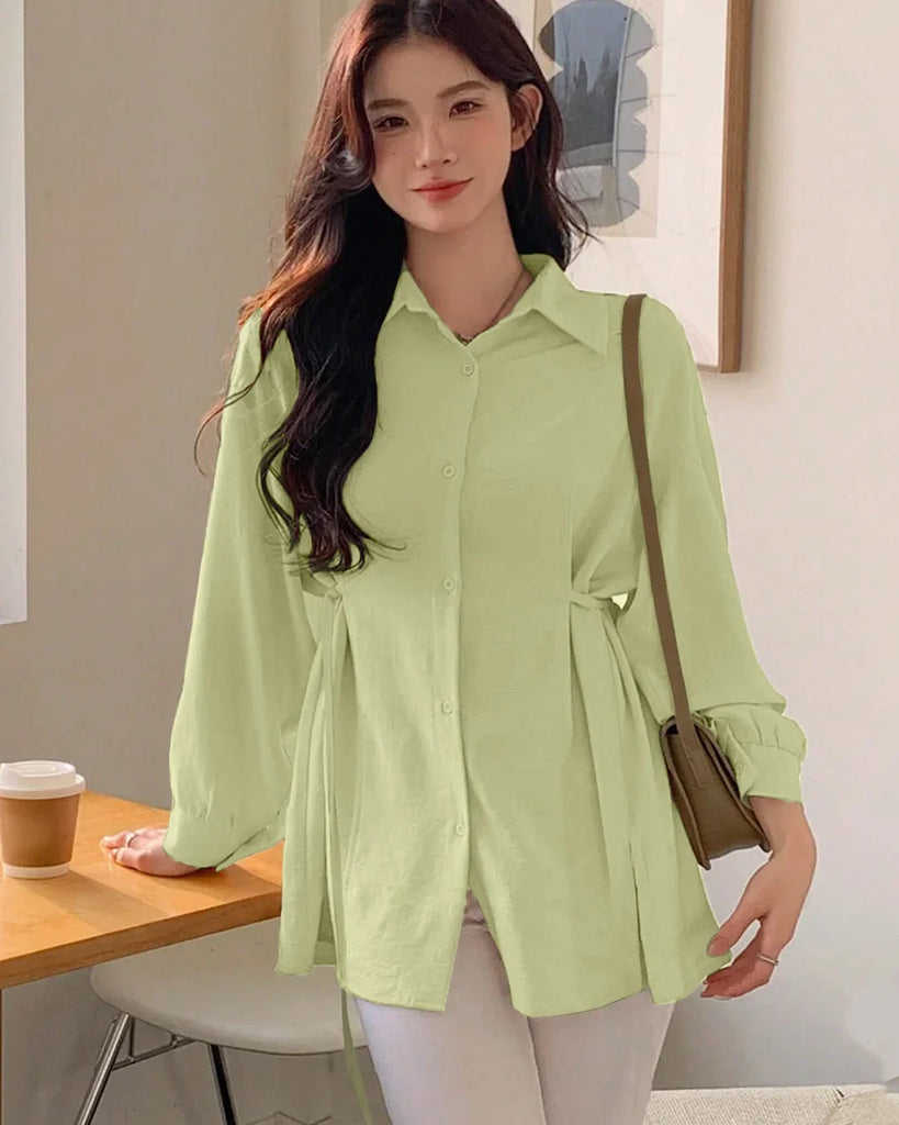  A woman in a green pleated button-down shirt and white pants, showcasing a stylish and casual outfit.
