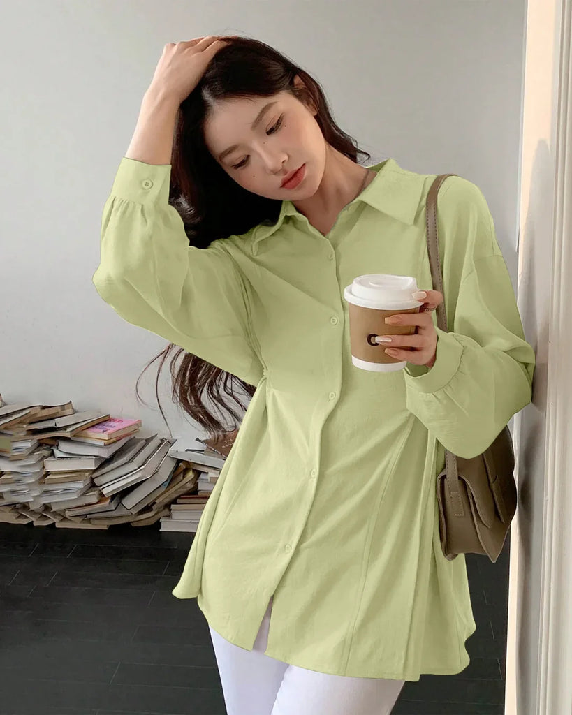 A woman in a green pleated button-down shirt and white pants, showcasing a stylish and casual outfit.