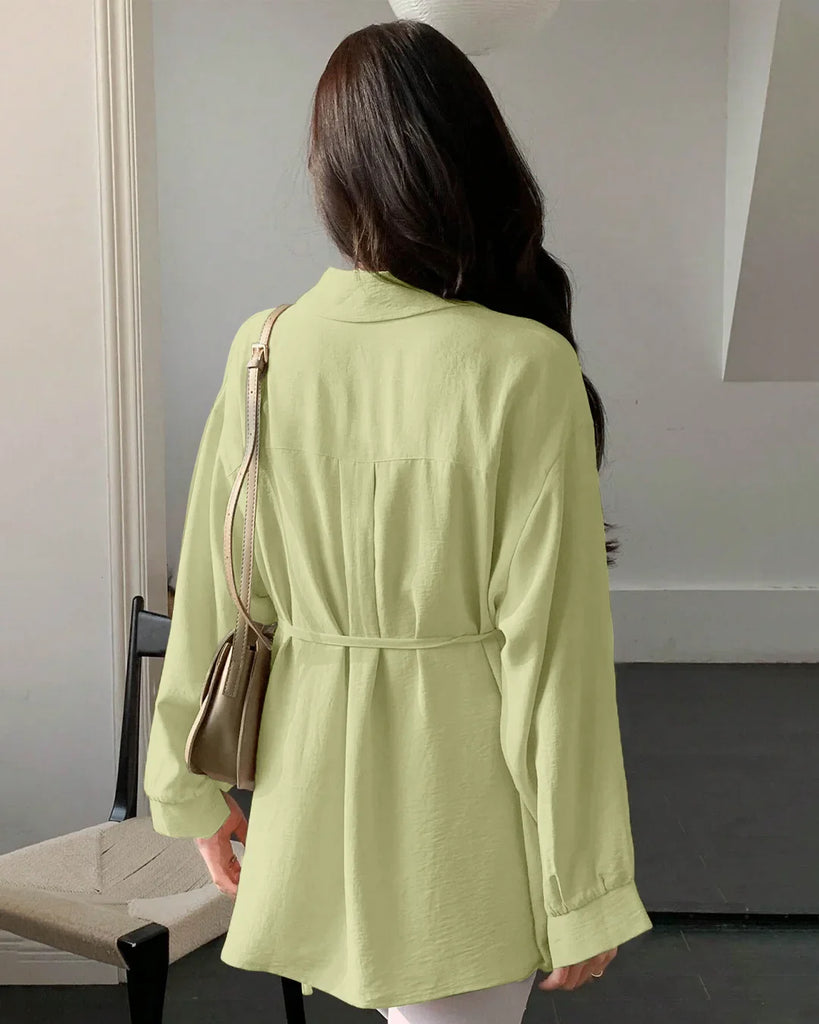 Back view of a woman in a green pleated button-down shirt and white pants, showcasing a stylish and casual outfit.