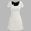 white mini dress featuring a round neckline, ruched design, and a stylish black bow tie accent