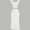  White dress featuring a ruched crop top and an asymmetric hem skirt with a ruffled design.