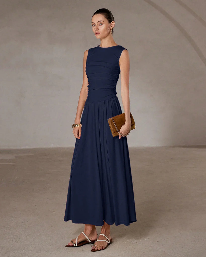 Model in a sleeveless navy blue maxi dress with a ruched waist, holding a stylish clutch.