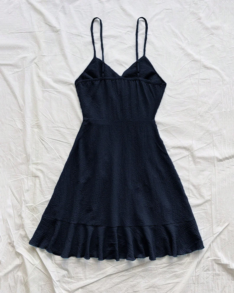 Back view of a navy blue ruffled wrap spaghetti strap dress paired with stylish sandals.

