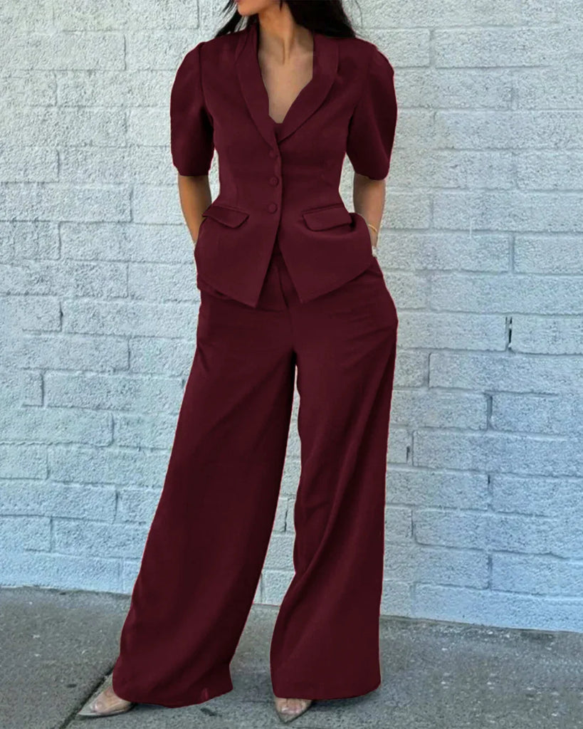 A woman wearing a short sleeve burgundy blazer and wide-leg trousers, complemented by high heels.