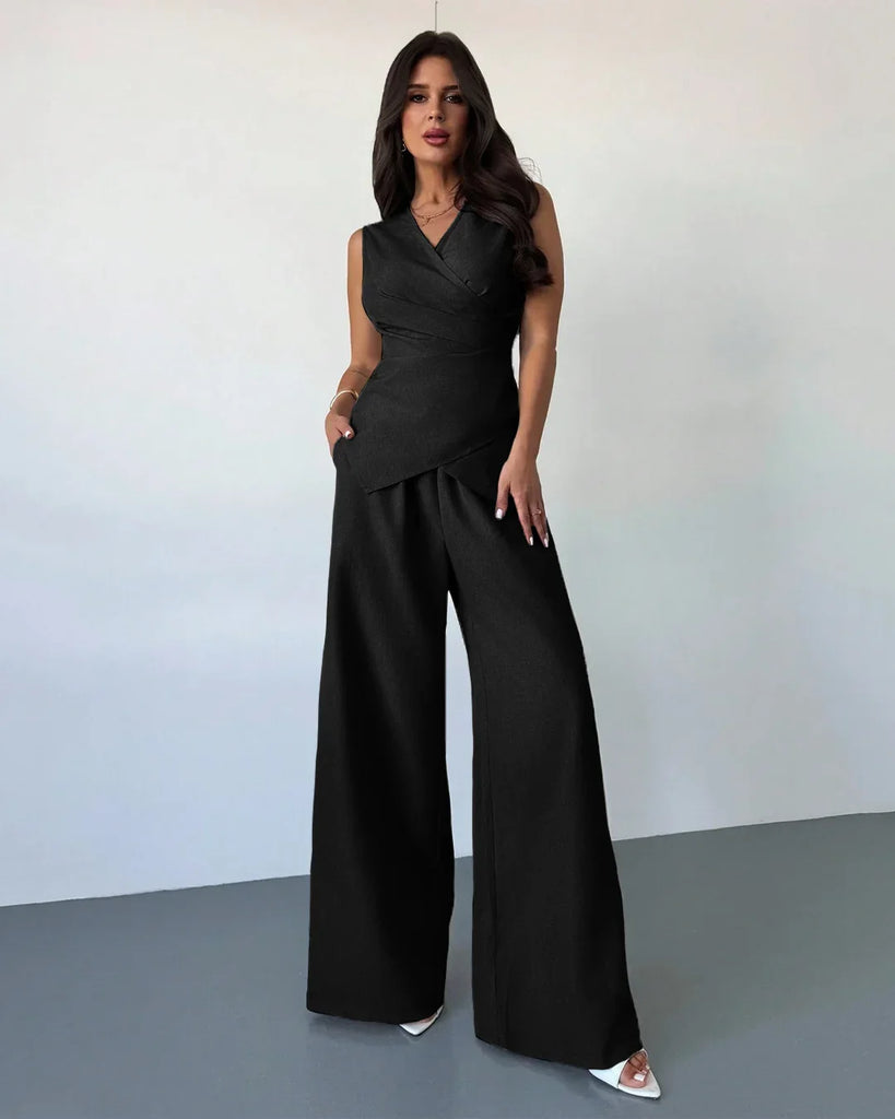 Model in a black sleeveless wrap top and wide-leg trouser matching set, showcasing a sleek and stylish look.

