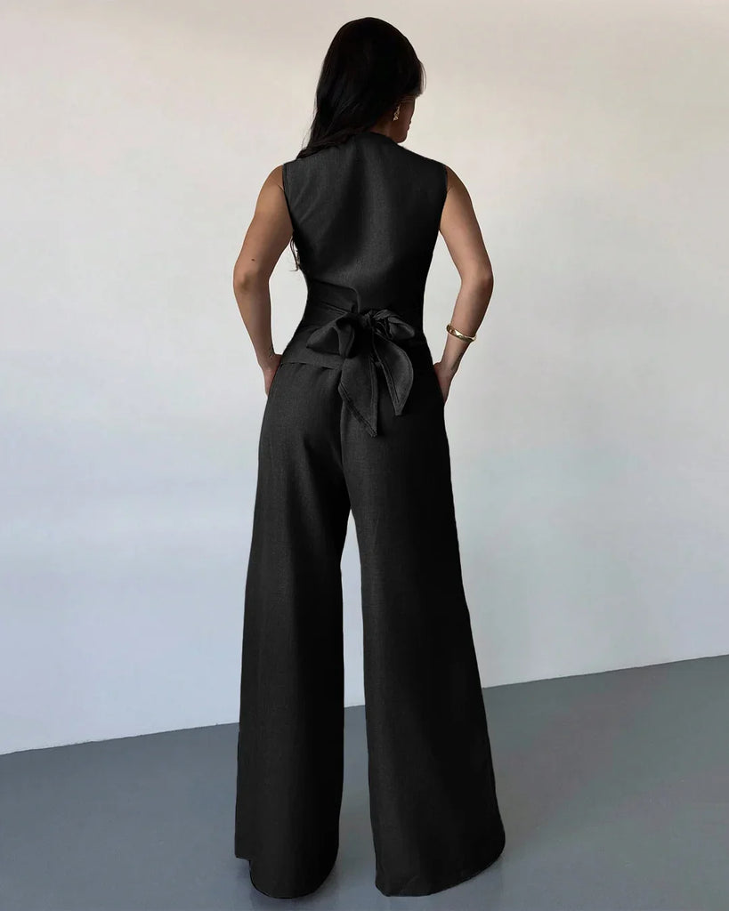 Back view of a Model in a black sleeveless wrap top and wide-leg trouser matching set, showcasing a sleek and stylish look.
