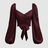 Burgundy top featuring a front bow, solid color, lantern sleeves, and a braided tie back with pleats.