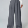 woman models solid grey wide-leg pleated trousers, showcasing a stylish and modern outfit