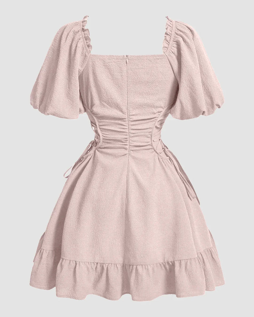 A powder pink dress featuring puff sleeves and ruffles, designed with a solid lace-up side detail.
