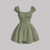 woman wearing waist cinched green dress with square neck texrured gracefully on a staircase