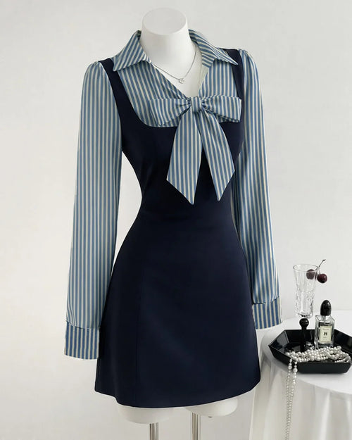 Front view of black pinafore dress with striped bow tie detail, long sleeves and fitted mini silhouette for a chic look.