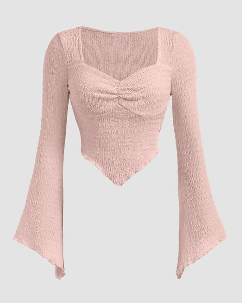 Front view of Model wearing light pink ribbed long sleeve top with flared cuffs and sweetheart neckline, paired with black pants.