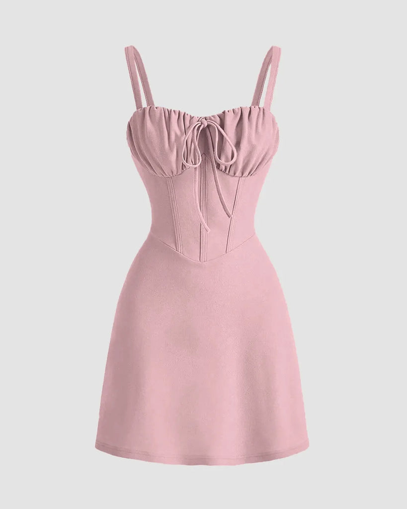 A woman wearing a dusty pink sweetheart neck mini dress and stylish sunglasses stands confidently.