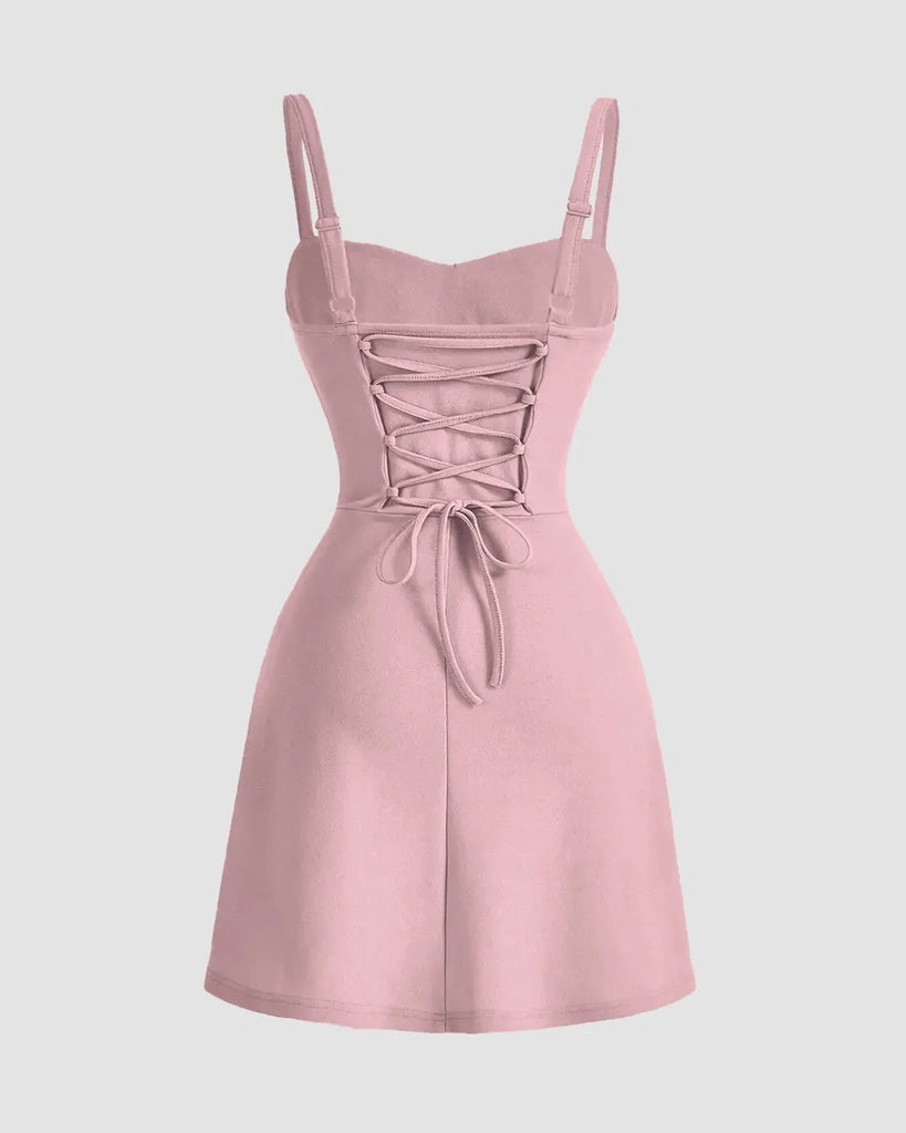 A woman wearing a dusty pink sweetheart neck mini dress and stylish sunglasses stands confidently.