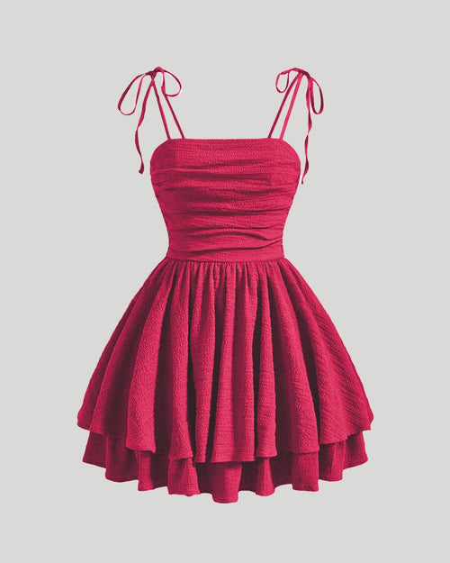 Red cami dress on a hanger, designed with tie shoulders and layered ruching for an elegant look.