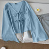 Front view of Light blue front bow tie top with V-neck design, flared long sleeves and soft textured fabric styled in a flat lay