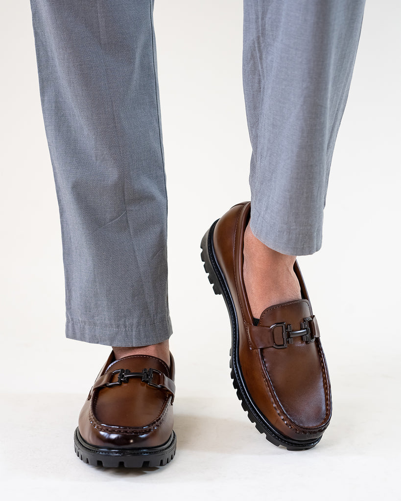 A model wearing grey pants and brown loafers 